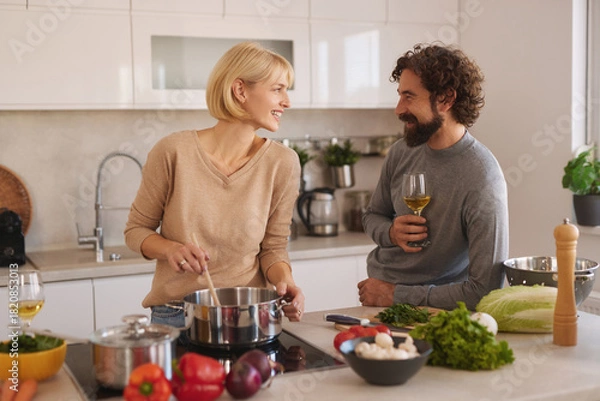 Fototapeta Two people are happily cooking in a bright kitchen. They are chopping vegetables and stirring a pot while enjoying each other's company and conversation.