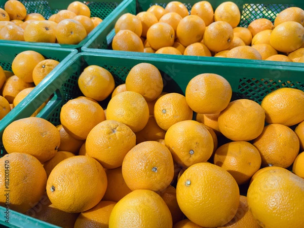 Fototapeta Bright orange oranges piled in green plastic crates at a supermarket produce section, showcasing fresh citrus fruits ready for sale in a grocery store.