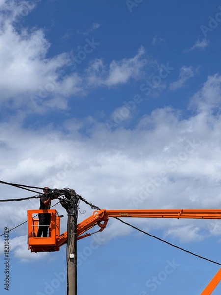 Obraz unrecognisable man electrician worker standing in an orange bucket crane repairing high voltage power line electrical cable outdoors