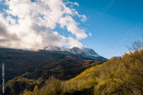 Fototapeta Snow capped mountain peaks emerging from clouds, an autumn landscape with colorful hillsides and clear blue sky, Gran Sasso, Abruzzo, Italy