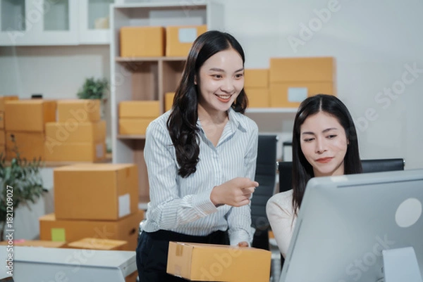 Obraz Two Asian women working together in an e-commerce office, managing online orders and shipping logistics while checking product details on a computer,demonstrating teamwork, entrepreneurship,business