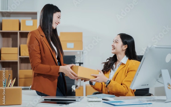 Fototapeta Asian female entrepreneurs coordinating product handover at an e-commerce office, preparing parcels for shipping logistics while collaborating professionally to manage online business operations