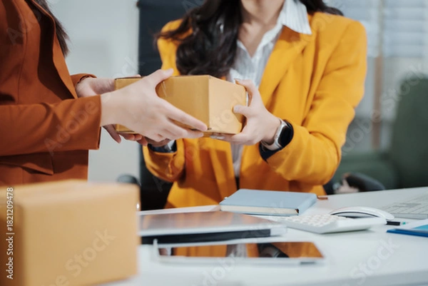 Fototapeta Asian female entrepreneurs coordinating product handover at an e-commerce office, preparing parcels for shipping logistics while collaborating professionally to manage online business operations