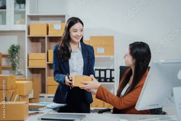 Fototapeta Asian female entrepreneurs coordinating product handover at an e-commerce office, preparing parcels for shipping logistics while collaborating professionally to manage online business operations