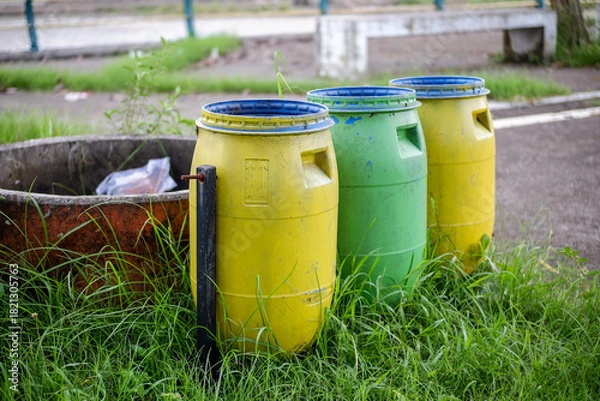 Fototapeta Colorful outdoor trash bins next to a sidewalk in a city park, Urban trash and recycling