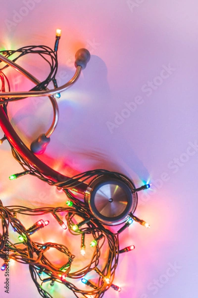 Fototapeta Red stethoscope with shining colorful Christmas lights on white background, vintage toned, medical holiday or Christmas in hospital concept