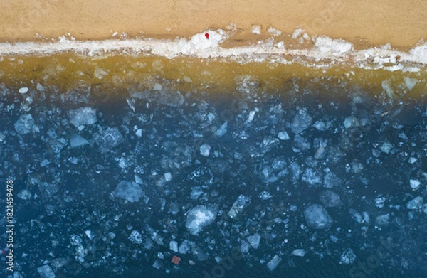 Fototapeta Aerial top down view of a frozen river bank with broken ice.