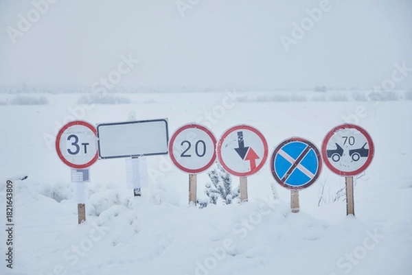 Fototapeta Road signs at an ice crossing in the snow across a river in winter