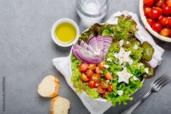 Fototapeta Cute green salad with mini cherry tomatoes, red onion slices and feta cheese stars. Top view copy space.

