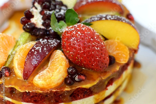 Obraz A slice of red velvet cake decorated with strawberries, pomegranate, and other fruits. Selective focus.