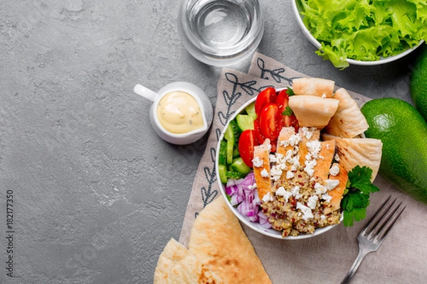 Fototapeta Healthy buddha quinoa salad bowl with tomatoes, cucumbers, red onions chicken and feta cheese. On grey concrete background. Top view copy space.

