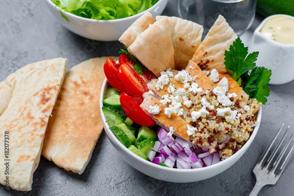 Fototapeta Healthy quinoa salad bowl with tomatoes, cucumbers, red onions chicken and feta cheese. On grey concrete background. Horizontal side view.

