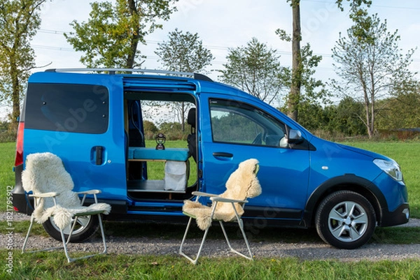 Fototapeta gemütlicher Minicamper steht im Grünen mit Stühlen davor 