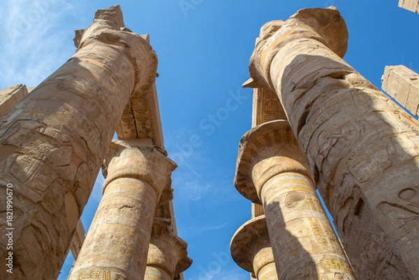 Fototapeta Egypt, Luxor, 01.02.2022.Tall ancient Egyptian temple columns decorated with colorful hieroglyphs and painted figures illuminated by bright sunlight, creating a warm historic atmosphere.