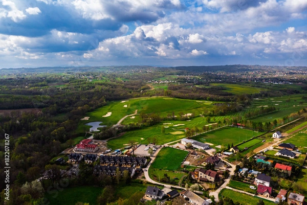 Obraz Wide aerial drone panorama of a lush green golf course on a bright, cloudy day. Featuring fairways, sand traps, and luxury resort facilities in the distance.