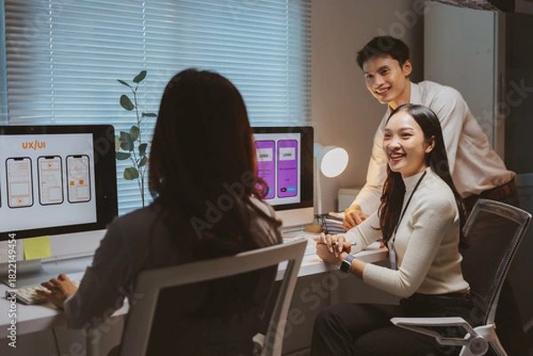 Fototapeta Asian UIUX designers and developers collaborating on a new mobile application interface, working together on a late night project