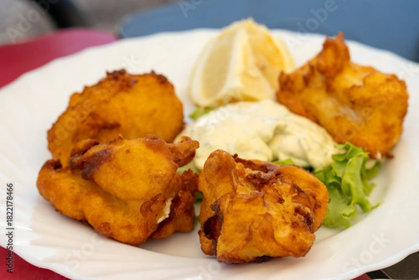 Fototapeta Dish with pieces of breaded and fried fish from the Canary Islands in a restaurant in Tebnerife, accompanied with tartar sauce and lemon