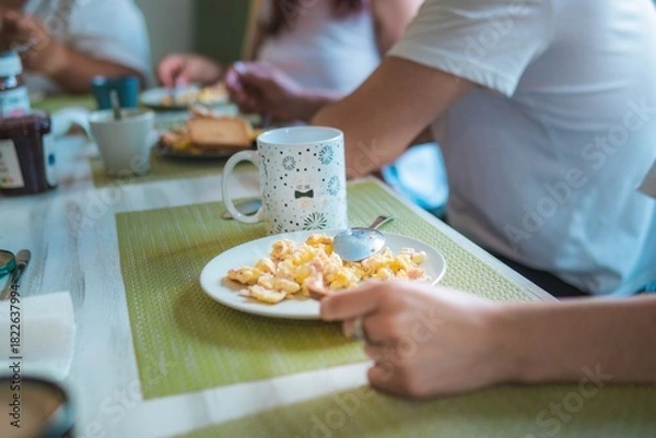 Fototapeta family having breakfast, only their hands and the plates on the table are shown