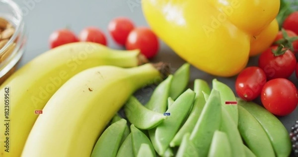 Fototapeta Displaying ripe bananas and green snap peas on gray counter, with tomatoes bell pepper nuts labels
