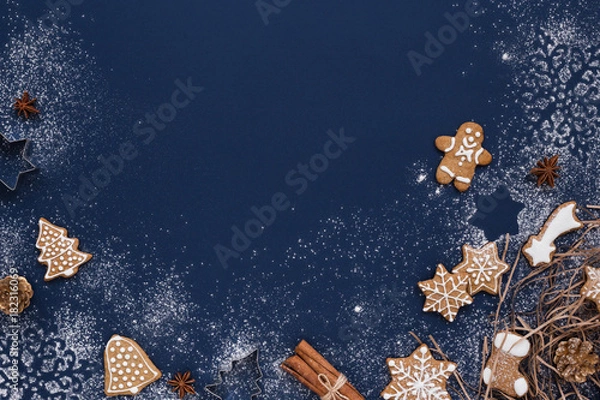 Fototapeta Christmas background with gingerbread and snow on navy colored surface. Holiday mood card. Top view, copy space.