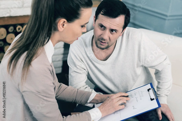 Fototapeta I will explain. Attentive man keeping mouth opened and wrinkling forehead while consulting with her