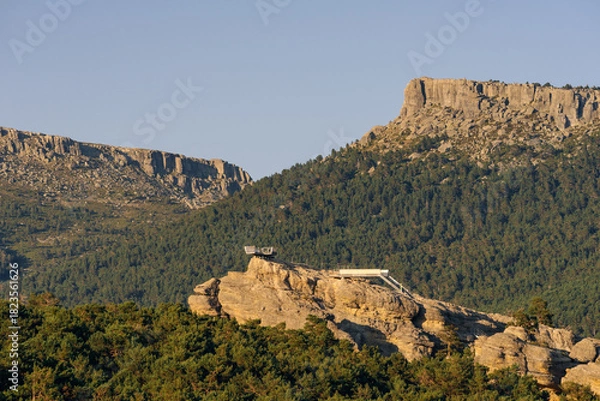 Fototapeta Walkways among rock formations and pine trees with the peaks of Urbion in the background in the Castroviejo nature reserve, in Duruelo de la Sierra, Soria, Castile and Leon, Spain.