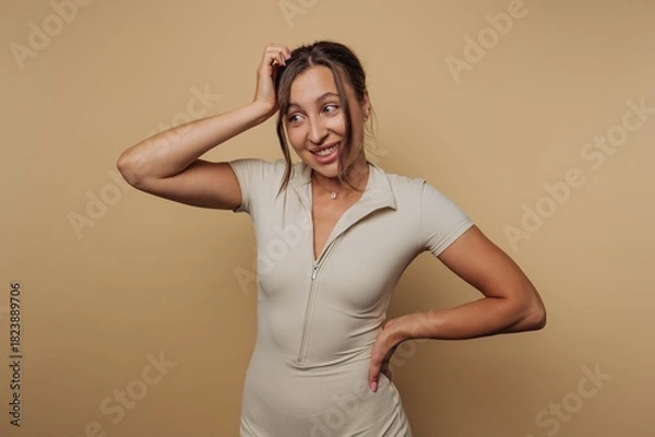 Fototapeta Smiling young woman with casual pose showing playful expression against a neutral background