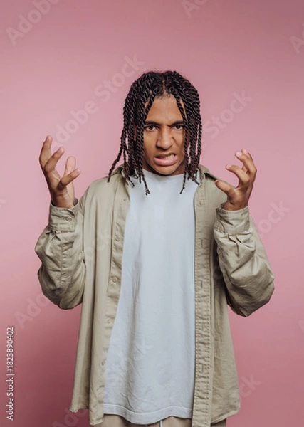 Obraz Portrait of young man expressing frustration with hands raised in front of pink backdrop