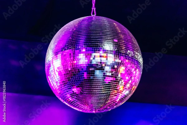 Obraz Close-up of a spinning disco ball illuminated by pink, purple, and blue lights inside a nightclub.