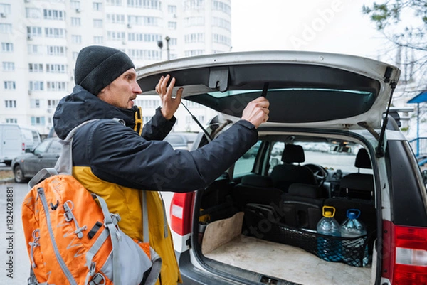 Fototapeta preparing vehicle for outdoor adventure, individual organizing backpacks and water bottles for outdoor trip, person arranging camping equipment and hydration supplies in vehicle before hike