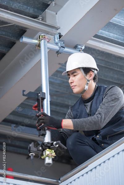 Obraz 天井が近い高所の足場で単管パイプを固定するクランプなどの施工作業　鳶職や作業員のイメージ　レンチで締め