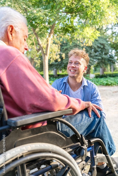 Obraz Young adult grandson enjoying conversation with senior man in wheelchair at park