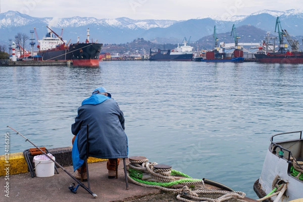 Obraz A fisherman fishes in the port of Batumi on a winter day in January.	