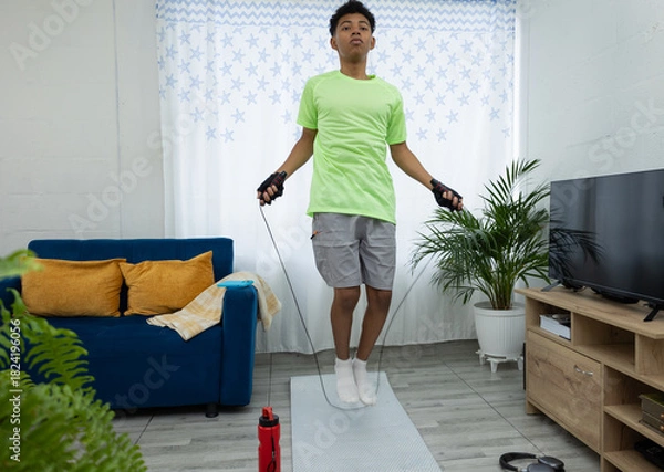 Obraz Brown skinned teenager jumping rope in his living room as part of his workout routine. Concept of home physical training