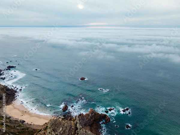 Obraz Aerial View of Secluded Beach and Rocky Shoreline Beneath Fog-Covered Atlantic Ocean at Cabo da Roca, Sintra, Portugal