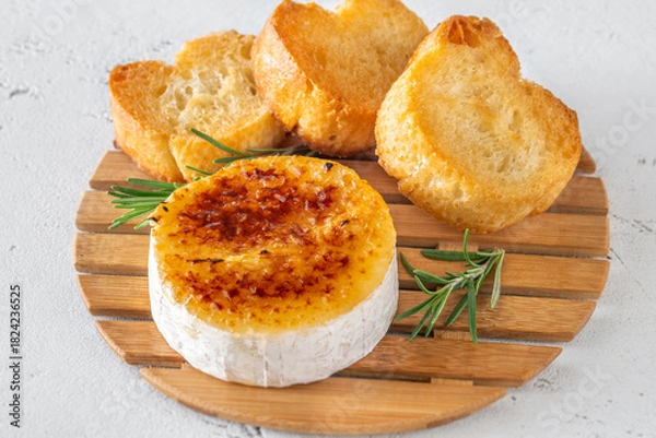 Fototapeta Flamed Camembert with caramelized golden sugar crust and fresh rosemary on board