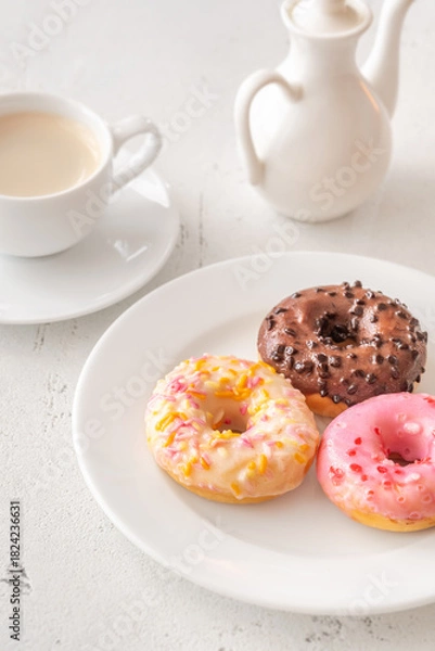 Fototapeta Trio of glazed donuts with coffee cup and pitcher in bright morning light