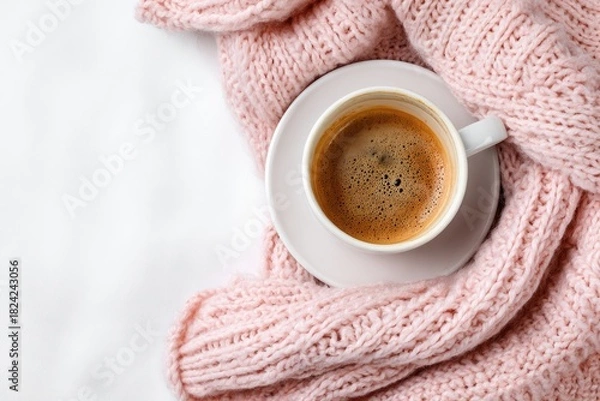 Obraz A cup of coffee on a white blanket, draped with a soft pink knitted throw