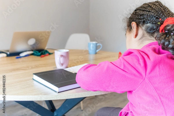 Obraz Young person engaged in learning or remote work, leaning over a notebook at a modern wooden table with a laptop, stationery, and hot beverages, emphasizing concentration and productivity