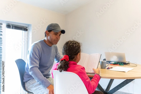 Obraz Father helping his young daughter with homework, supporting her learning and academic development, sitting together in a focused home study environment