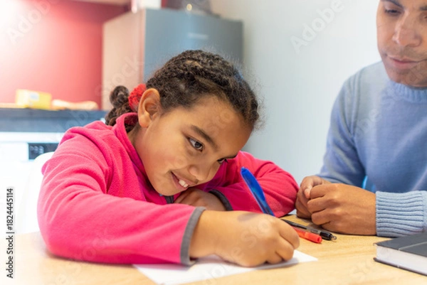 Obraz Young girl learning and developing her skills at home, her father supervising and supporting her while focusing on homework or creative activity