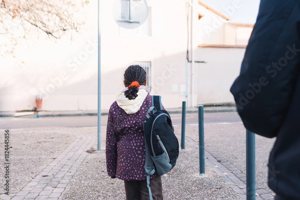 Obraz Young student girl with a backpack walking on the street, back to school concept, child on her way to elementary school, beginning of education journey