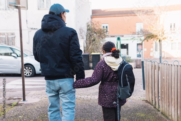 Obraz Father and daughter walking hand in hand on a city street, going to school, symbolizing family bonding, care, safety, and guidance in urban setting