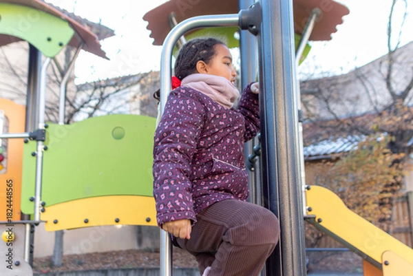 Obraz Young biracial girl in warm clothing actively climbing stimulating playground equipment, engaging in physical activity and fostering growth through outdoor play