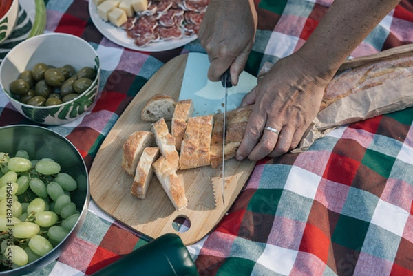 Fototapeta Hands of an unrecognizable person slicing baguette for a family picnic outdoors