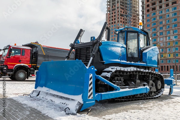 Obraz A blue bulldozer and a dump truck at a construction site in winter