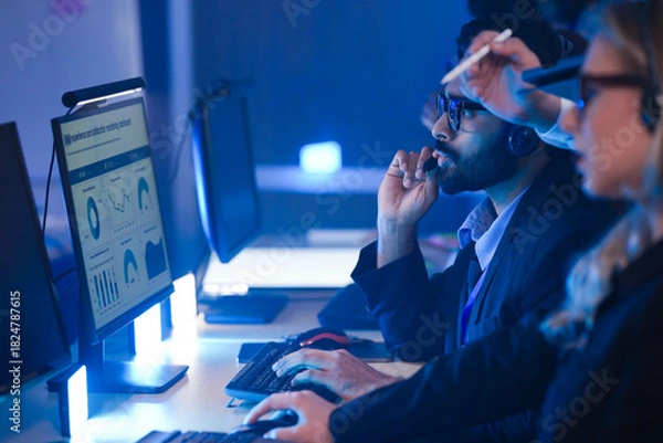 Fototapeta Indian cybersecurity analyst utilizing AI voice interface for real-time threat detection in a smart city command center, collaborating on cloud infrastructure defense.