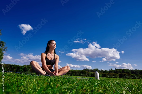Obraz Girl sits in Park on a background of clear sky and enjoy the sunlight.