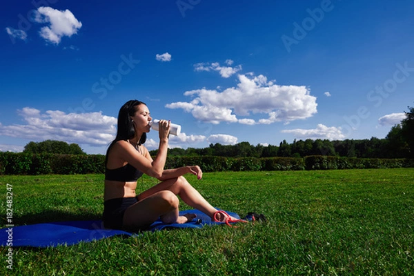 Obraz Girl sits in Park on the grass on a Sunny day and drinking water.
