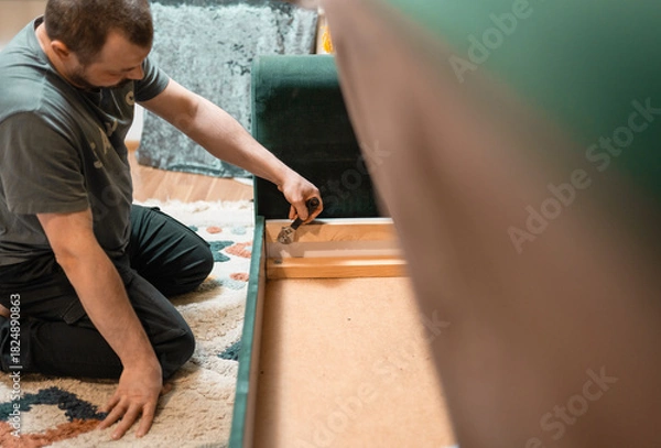 Fototapeta Man disassembling sofa furniture mechanism at home using furniture wrench. DIY Assembling Furniture concept.